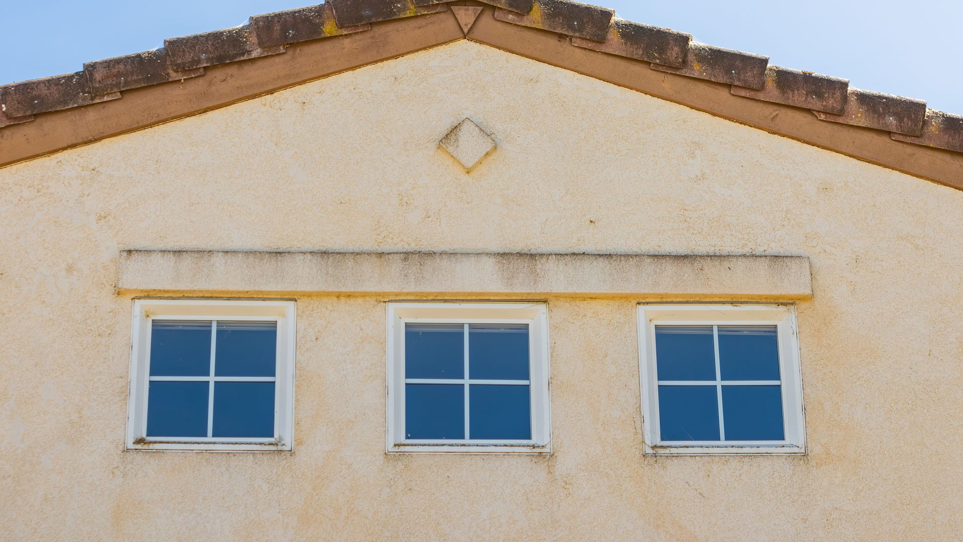 Close-up view of a house facade featuring three evenly spaced glass windows under a triangular roof in Riverside, CA